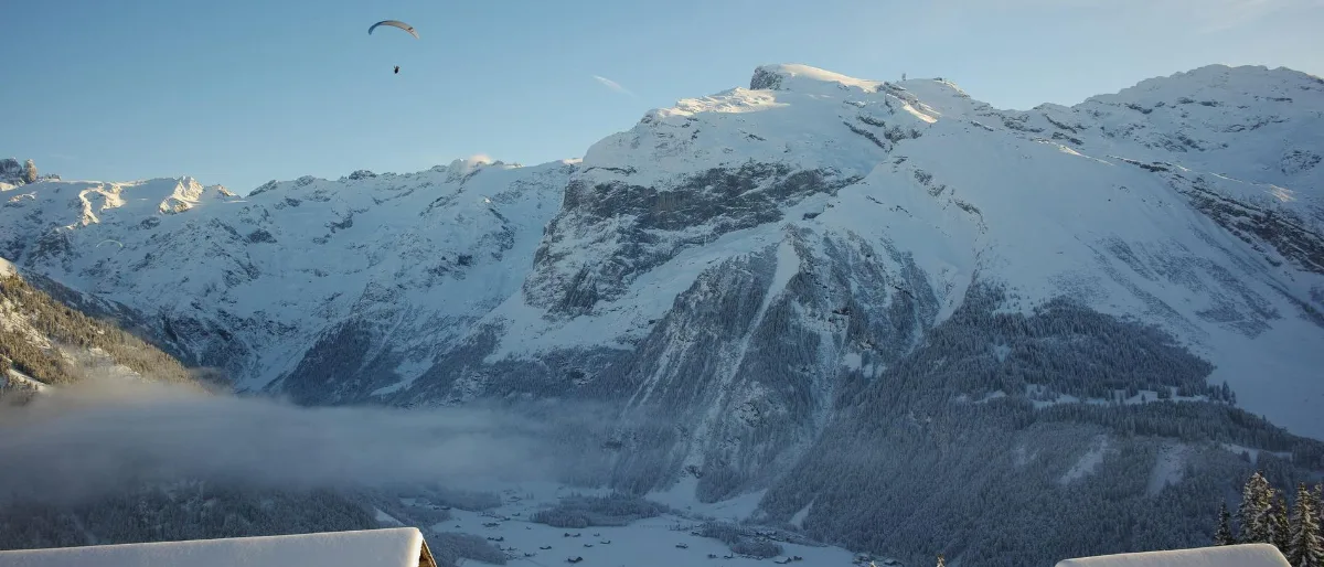 The Engelberg valley in summer with the Titlis massif behind and a paraglider in the sky.
